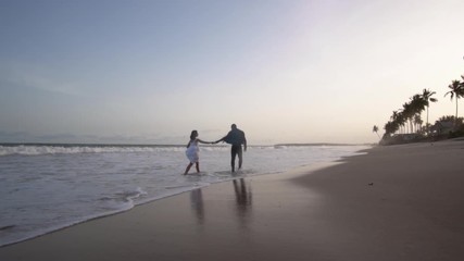 Interracial couple in love having a romantic stroll at sunset along a paradisiacal beach and kissing