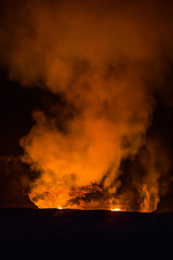 As darkness of night envelopes the crater, smoke and fire rise at Kilauea volcano.