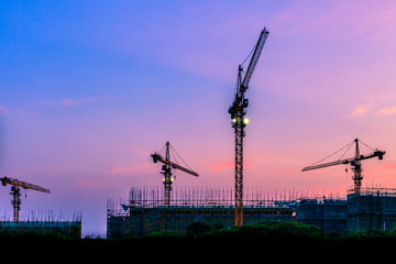 Tower crane and building construction site silhouette at sunrise.