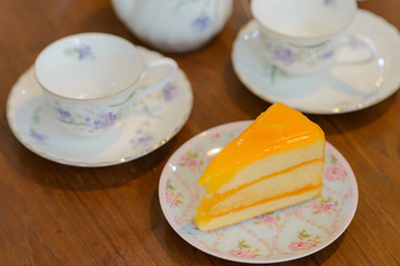 piece of delicious orange cake with teapot and cup of tea on wooden table