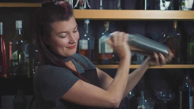 Female bartender shaking craft cocktail in bespoke speakeasy bar.