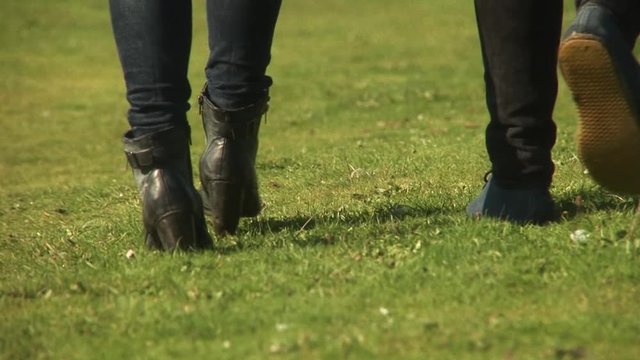 Couples footsteps walking away into distance holding hands bright sunny outdoor park grass field rear reverse low angle long shot
