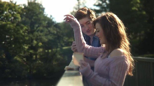 Happy cheerful smiling young couple playfully throwing bread feeding ducks from bridge on warm sunny day at park medium profile side shot slow motion