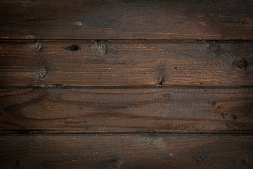 Dark brown surface of an old wooden floor, wall or table with cracks and knots. Dark rough weathered wood with vignette.