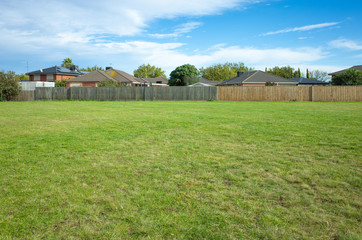 Obraz premium Background texture of a large public local park with green and healthy grass and with some trees and residential houses in the distance. Melbourne, VIC Australia
