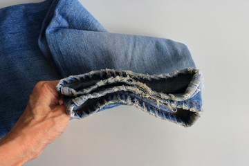 Hand holding frayed legs of a pair of faded jeans, selective focus