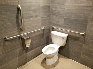 A clean restroom with handicapped railings and grey tiles on the wall