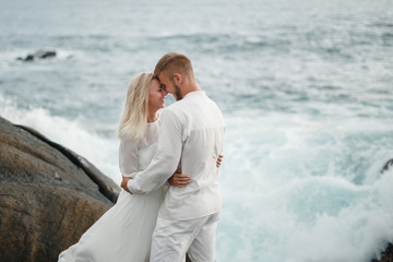 Beautiful wedding couple on the beach , kissing couple. Groom hugs bride's shoulders while kissing her on the shore