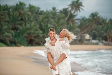 Groom holding bride on his back. Happy Romantic honeymoon couple on the beach, honeymoon in Sri...