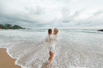 Groom holding a bride in front of he ocean. Back view happy just married couple at the sea
