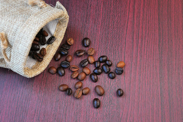 Coffee beans falling from a sack bag on a wooden background.
