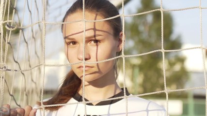 Portrait of young serious woman football player wearing uniform looking into camera in soccer gate at sport field. World Cup Game