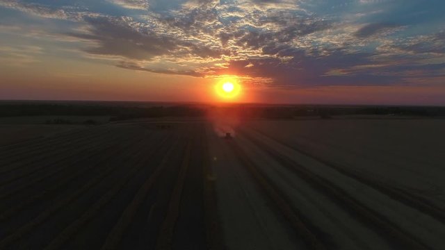 Drone flying upwards above a combine on a canola field during sunset