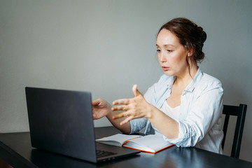 Adult brunette woman reads terrible news at opened laptop at the table