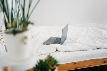 Opened laptop notebook on bed at bright scandinavian interior, work from home freelance concept