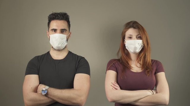 Isolated couple with surgical Mask, standing and facing at camera in studio, during covid-19 pandemic virus in France. 4K UHD. Two young persons. Disease Prevention. Social Distance in relationship.