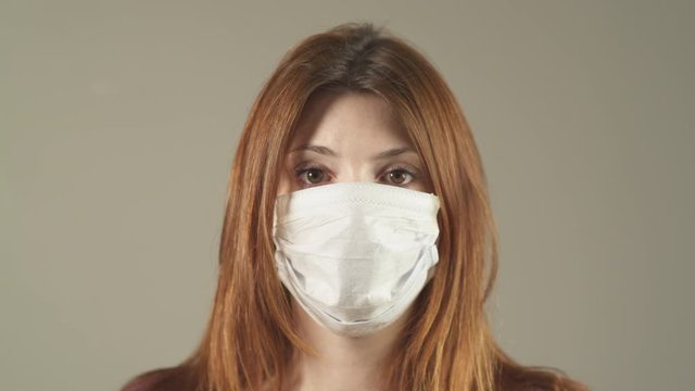 Close-up of Isolated woman with surgical Mask, red hair and shirt standing and facing at camera in studio, during covid-19 pandemic virus in France. 4K UHD. One person young girl. Prevention.