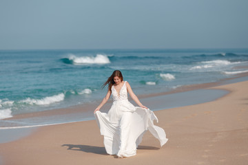 Fototapeta na wymiar Bride walking along sea coast in the wedding dress. Bride walking along tropical sand beach wearing beautiful wedding dress