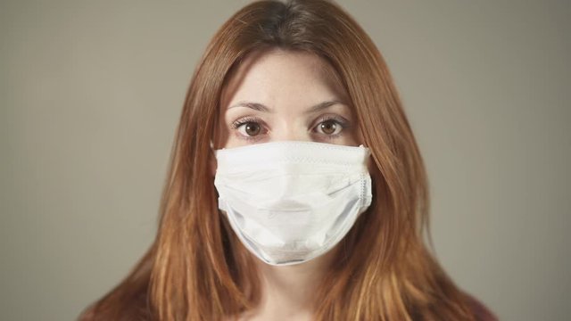 Isolated Masked caucasian woman, redhead and freckles, red hair and shirt standing and facing at camera in studio, during covid-19 pandemic in France. 4K UHD. One person young girl in close-up shot.