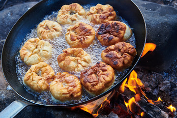 Cooking fishcakes in a pan on a fire.