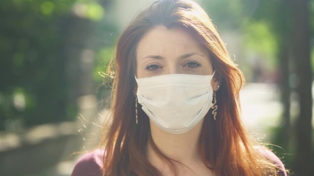Close-up of Isolated Masked caucasian woman, redhead and freckles, red hair and shirt standing and facing at camera outside in street, during covid-19 pandemic in France. 4K UHD. One person.