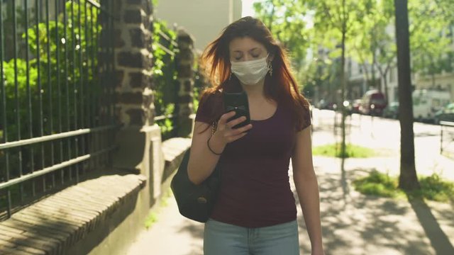 Attractive woman with surgical mask, redhead and freckles, red hair and shirt walking outside in street, during covid-19 pandemic in France. 4K UHD. One person chilling on social media.