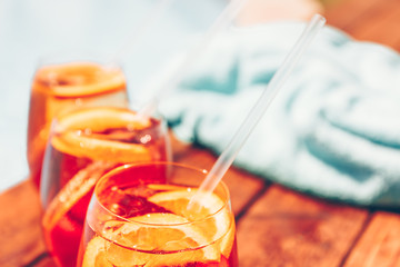 Three glasses of aperol spritz and negroni cold cocktail with straws on wooden edge of swimming...