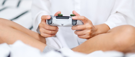 Closeup image of a woman holding game controller while playing games , sitting on a white cozy bed at home © Farknot Architect