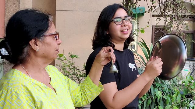 Young & old Indian women making noise with a plate & spoon & bell as a mark of respect for essential healthcare workers, medical personel, doctors, policemen during the coronavirus lockdown in India