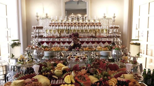 A large, beautiful, delicious buffet with lots of fruits and alcoholic beverages in blue and white, in crystal glasses, is waiting for guests on a festive day. Panoramic shooting, close-up.