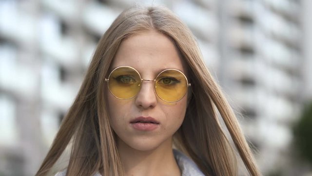 4k. Young long hair girl in sunglasses stand in city street and look at camera. Close up portrait 