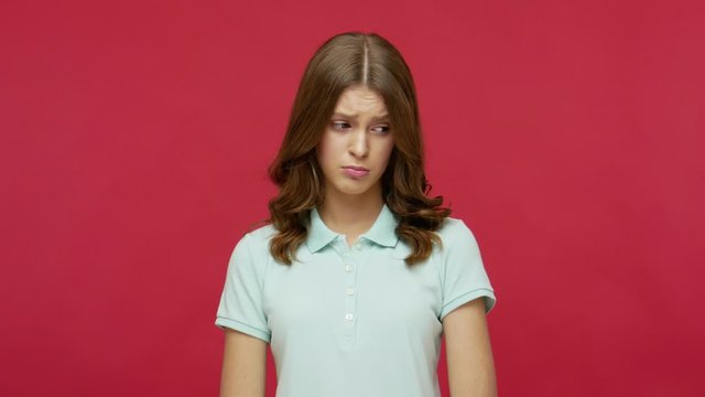 Unhappy woman in polo t-shirt sighing, looking resentful and sad at camera, bowing head with gloomy worried expression, feeling depressed frustrated. indoor studio shot isolated on red background