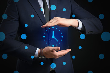 Businessman with virtual clock on dark background. Time management concept
