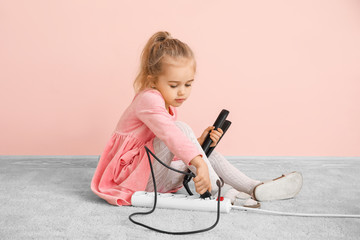 Little girl playing with electric extension cord and hair iron at home