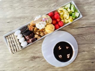 Chocolate fondue sauce dipped with fruits and confectionary snack on wooden background, top view