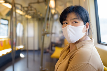 Overweight Asian woman with mask thinking while sitting with distance inside the train