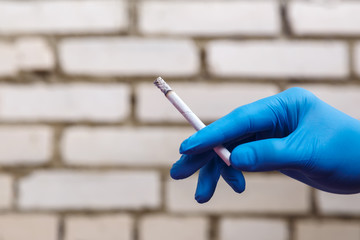 A hand in a blue rubber glove holds a cigarette