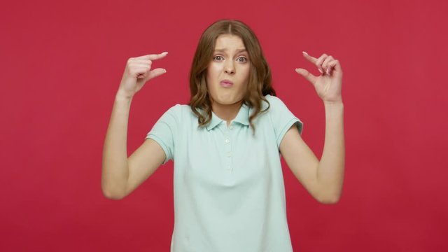 Small amount, low rating. Young brunette woman in t-shirt making little bit gesture, showing tiny size, looking sceptic and disappointed with minimum. indoor studio shot isolated on red background