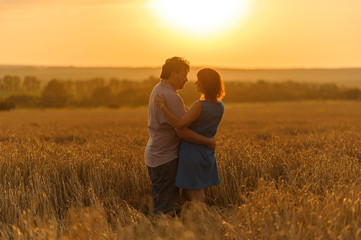 An adult farmer and his wife are hugging in their wheat field.