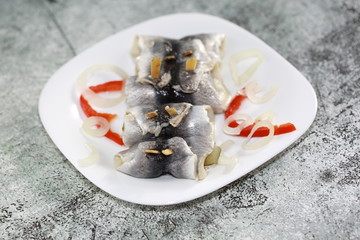 Pickled herrings called rollmops with pieces of onion and red pepper on plate on marble table 