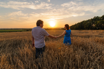 An adult farmer and his wife are walking hand in hand through their wheat field.