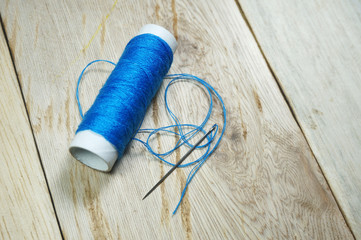 Blue threads and sewing needles on the wooden table. Selective focus to sewing needle                   