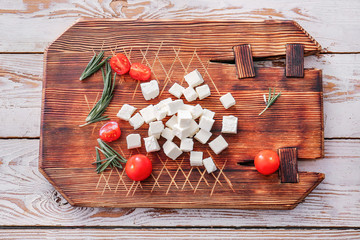 Board with tasty cut feta cheese, tomatoes and herbs on table