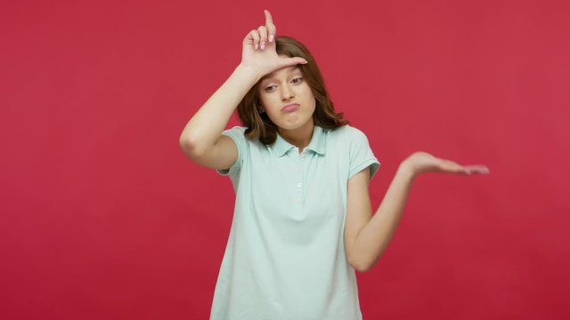 I lost, my failure. Upset young brunette woman in polo t-shirt making loser gesture, L sign on her head and looking with frustration, depressed about defeat, unsuccess. indoor studio shot, isolated