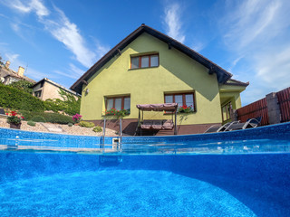 small home swimming pool with two black sun loungers and rocking bench. Underwater split screen view. Covid 19 - Summer 2020 holiday concept. Vacation at home