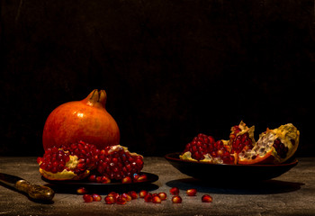 Two pomegranates, one whole, the other broken into segments  on a dark rough surface. Still life. Light painting technique. © Tatiana Sidorova