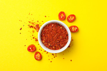 Chilli pepper and bowl of spice on yellow background
