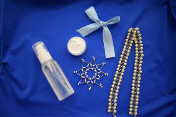 Cosmetics for makeup, and a snowflake necklace on a blue background. The view from the top.