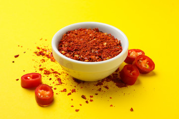 Chilli pepper and bowl of spice on yellow background