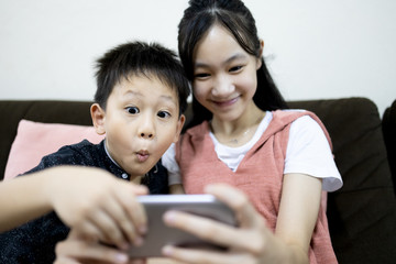 Excited kid boy and child girl are enjoying playing online game on mobile phone,siblings having fun relaxing together,children sister and brother using smartphone to watch cartoon video,stay home